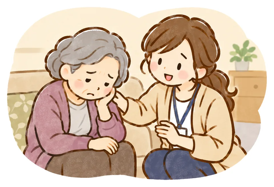 うつむくおばあさんの隣でケアマネがしゃがみ、そっと肩に手を添えている